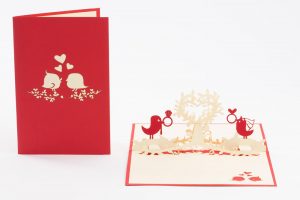 Love Birds holding wedding rings on a heart shaped flower. 3D pop up greeting card. Open and front view.