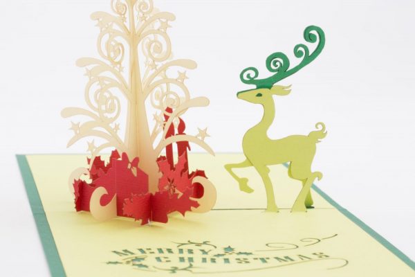 (Card open, close up)A reindeer standing beside a majestic Christmas tree