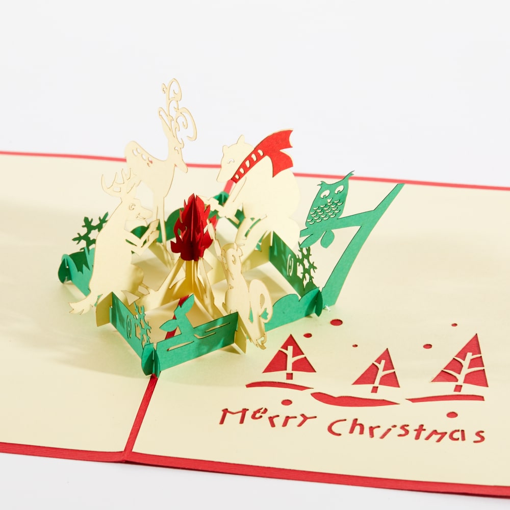 Christmas 3D pop up greeting card: A 3D Christmas scene with a reindeer, whit tailed deer, owl and squirrel sitting around a campfire.